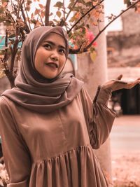 Smiling young woman looking away while standing by tree