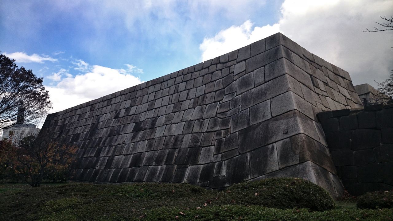 architecture, built structure, building exterior, sky, low angle view, cloud - sky, history, wall - building feature, cloud, old, tree, day, stone wall, text, no people, outdoors, cloudy, brick wall, western script, building