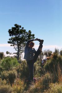 Full length portrait of woman standing on one leg at field against clear sky