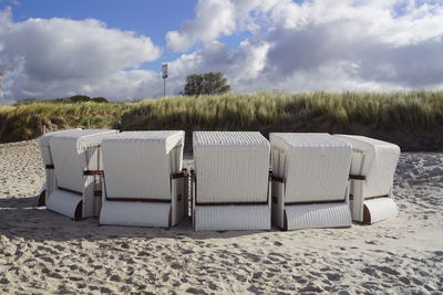 Hooded beach chairs on sand against sky