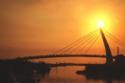 Silhouette bridge over river against orange sky