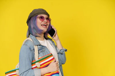 Young woman standing against yellow background