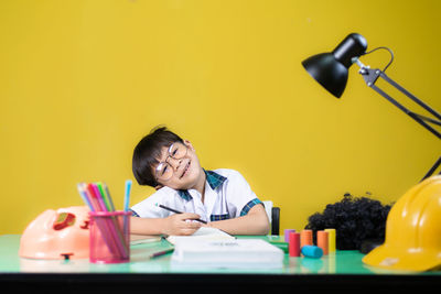 Portrait of smiling girl sitting on table against yellow wall