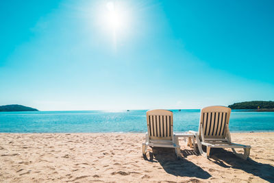 Deck chairs at beach against sky