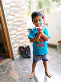 Cute boy holding pinwheel toy on floor at home 