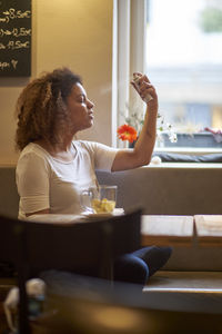 Young woman spraying perfume while sitting in restaurant
