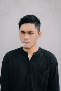 Portrait of young man smoking while standing wall