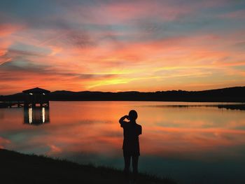 Silhouette man standing by lake against sky during sunset