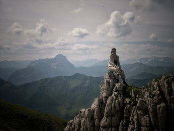 Woman sitting on mountains against cloudy sky