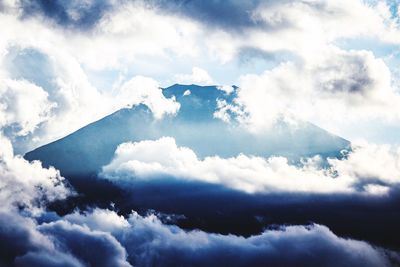 Low angle view of clouds surrounded by mountains against cloudy sky