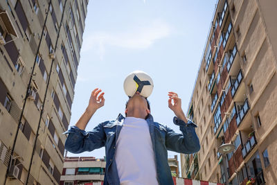 Low angle view of young man playing with football against sky during sunny day