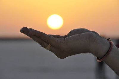 Close-up of hand against sea during sunset