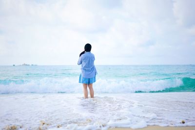 Rear view of woman standing at beach against cloudy sky