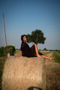 Full length of woman sitting on haystack on field