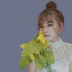Portrait of woman holding yellow while standing against gray background