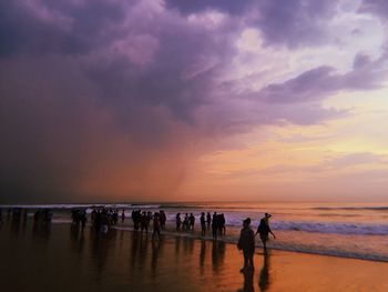 People on beach against sky during sunset