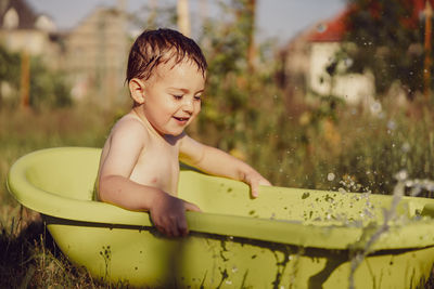 Cute little boy bathing in tub outdoors in garden. happy child is splashing, playing with water