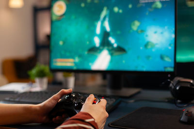 Cropped hands of woman playing video game at home
