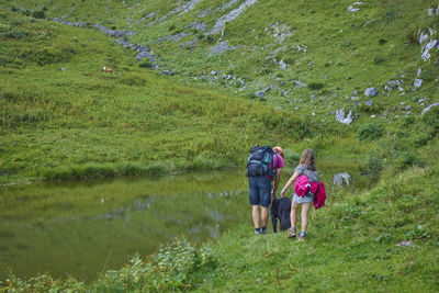 Rear view of daughter with father by pond at hills