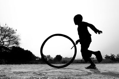 Side view of silhouette boy playing on field against clear sky