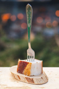 Piece of lard or bacon skewered with a fork on a wooden cutting board, close up, vertical