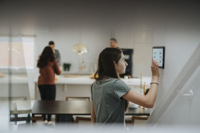 Girl using digital tablet mounted on wall by family at modern home