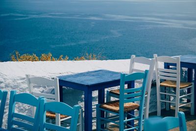 Empty chairs and tables by sea against sky