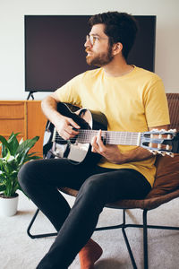 Man looking away while playing guitar at home