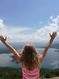Rear view of girl with arms raised standing against lake