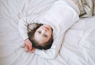 Cuty funny little girl with long hair in white home dress having fun lies on bed at home