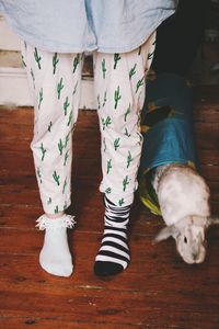 Low section of person wearing socks while standing by rabbit on hardwood floor