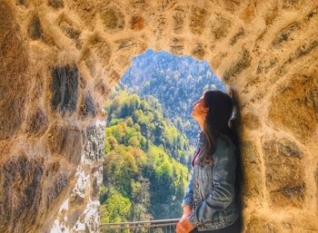 Side view of woman standing in doorway of cave while looking at view