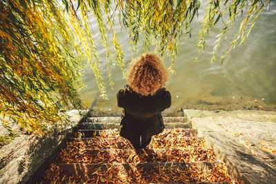 Rear view of woman standing on leaves covered steps in front of pond