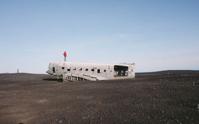 Person standing on crashed airplane on black sand against sky