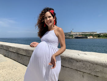 Portrait of smiling young woman standing at sea against sky