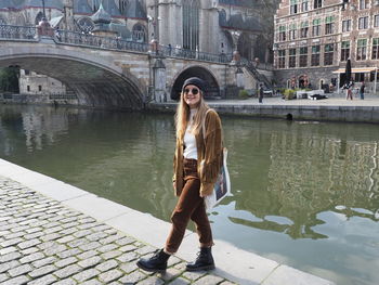 Portrait of young woman standing on bridge over canal