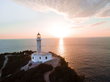 Lighthouse by sea against sky during sunset