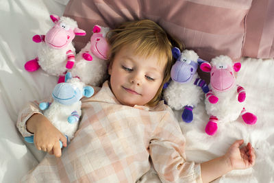 Smiling girl with toys lying on bed at home