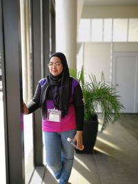 Smiling woman wearing hijab while standing by door