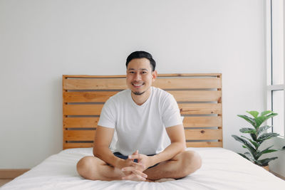 Portrait of young man sitting on bed at home