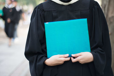 Midsection of woman wearing graduation gown holding document