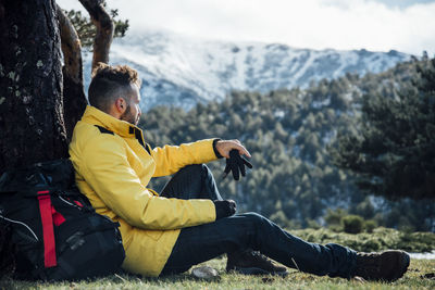 Young man with yellow jacket and backpack sitting on the mountain.