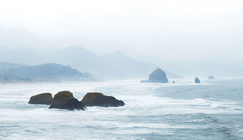 Rock formation in sea against sky during foggy weather