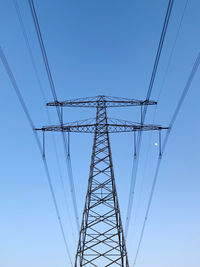 Low angle view of electricity pylon against clear blue sky