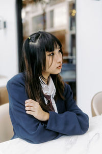 Young woman looking away while sitting on sofa at home