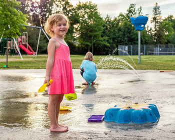 Little children playing with water and toys at splash pad in public park playground in summer