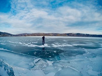 Woman standing in frozen lake against sky