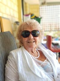 Portrait of smiling senior woman wearing sunglasses while sitting at home