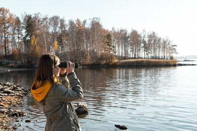 Rear view of woman photographing by lake against sky
