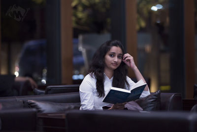 Portrait of young woman reading book in lobby
